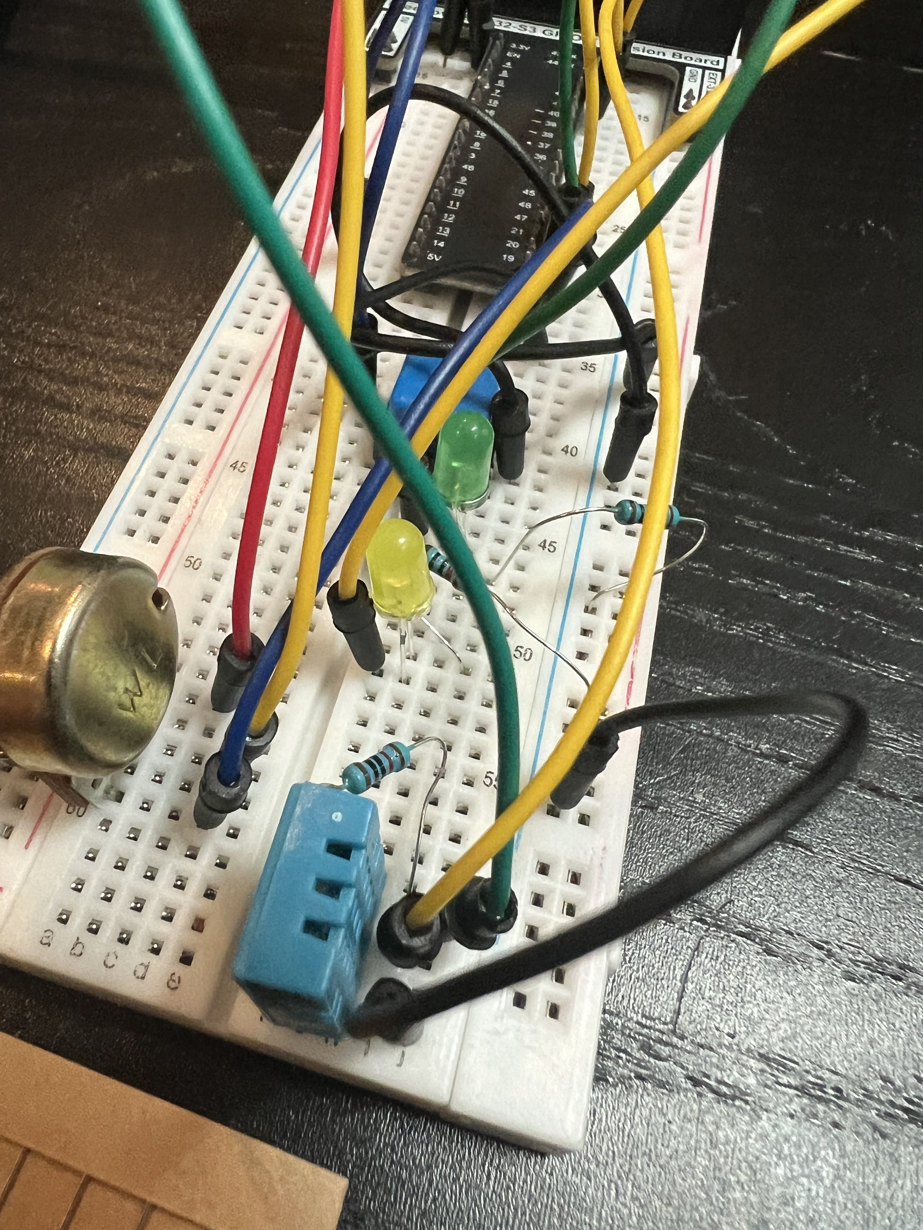 ESP32-S3 environmental monitor on a breadboard with a blue DHT11 sensor, LEDs, resistors, potentiometer, and jumper wires